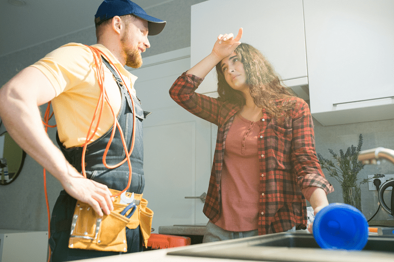 Exhausted young woman holding plunger while talking to young plumber